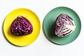 From above of halved red cabbage placed on yellow and green plates on white background