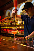 Young Asian bartender pouring grapefruit juice in the glass while preparing a cocktail in the bar