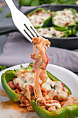 Fork with delicious homemade baked pizza stuffing with melted cheese served in green bell pepper on white plate in kitchen