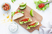 Small delicious tacos with red caviar and green lettuce served on wooden cutting board on table