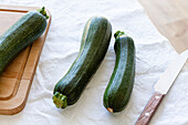Draufsicht auf frische, reife Zucchini, die mit Messer und Schneidebrett auf dem Tisch liegen und für die Zubereitung einer Cremesuppe zum Mittagessen vorbereitet werden
