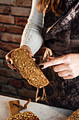 Anonyme Bäckerin demonstriert weiches frisches Brot mit knusprigen Kernen am Tisch in einer Bäckerei