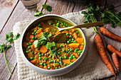 Draufsicht auf Schüssel mit köstlichem Carry-Gericht mit Gemüse, gekrönt mit grünen Basilikumblättern, serviert neben Topf auf Tisch mit rohen Karotten