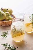 From above of cold pear cocktail in glasses with rosemary and ice cubes placed on table with fresh fruits