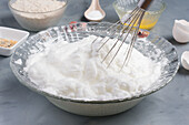 Glass bowl with fresh whipped white white with whisk placed on table with various ingredients during cooking process in kitchen