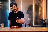 Koch gießt mit Gewürzen Fleischröllchen mit Soße auf stilvollem Teller in Ramen-Bar