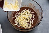 From above of crop anonymous cook adding grated butter into bowl with chocolate sweet waffle batter during cooking process in kitchen