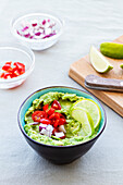 High angle of bowl with tasty guacamole with ripe cherry tomato and red onion near lime slices