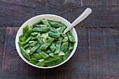 Blick von oben auf gesunden Salat mit grünen Bohnen und Knoblauchscheiben in einer Schüssel auf einem Holztisch