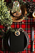Holiday place setting with empty menu and wooden ornament, on checkered red tablecloth, on the christmas table, defocused lights.