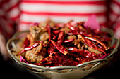 Frauenhände halten Korbschüssel mit Hähnchen-Chili-Paprika-Gericht
