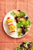 Top view of fresh vegan plate with vegetable skewer and marinated tofu served with a mixed lettuce salad