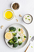 Blick von oben auf schmackhaften Brokkoli mit frischer Zitrone und Soße neben Schalen mit Olivenöl und Gewürzmischung auf dem Tisch