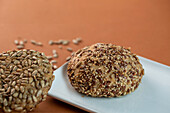 Delicious fresh buns with various seeds served on ceramic plate against brown background