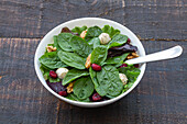 High angle of delicious salad with spinach and beans and walnuts served in bowl on wooden table for healthy lunch