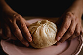 Hands of middle aged woman putting steamed baozi bun on ceramic plate