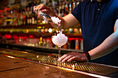 Hände eines nicht erkennbaren Barkeepers, der bei der Zubereitung eines Cocktails in der Bar zerstoßenes Eis in einen Becher gibt