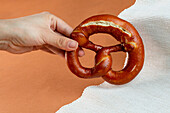 Unrecognizable female baker demonstrating delicious freshly baked pretzel with dark crust served on ribbed fabric against brown background