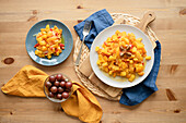 Draufsicht auf einen köstlichen frischen gesunden Salat mit reifen Kürbissen, roter Paprika und Kirschtomaten auf Tellern auf einem Holztisch in der Küche