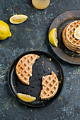 Halves of round tasty homemade baked sweet cheese waffles served on black plate with sour lemon and zest in light kitchen