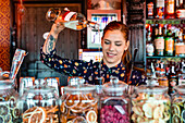 Female barkeeper pouring alcohol in shaker while preparing refreshing cocktail at counter in bar and looking away