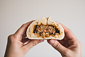 Hands of middle aged holding cut steamed baozi against plain background