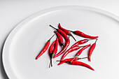 High angle composition of hot red chili peppers arranged around plate against white background