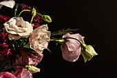 Frischer Blumenstrauß mit Rosen, weißen Lilien, Eustoma und Astern in einer Glasvase bei Sonnenschein
