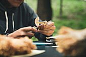 Crop unrecognizable person sitting at table and cutting fresh mushroom against green grass in nature