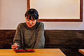 Junge asiatische Frau im Pullover isst an einem Holztresen in einem Cafe