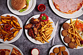 Draufsicht auf Teller mit verschiedenen Junkfood-Gerichten, die während des Mittagessens auf einem grauen Tisch neben Schüsseln mit Soßen stehen