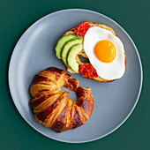 Plate viewed from above with croissant and an avocado egg toast