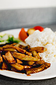 Nahaufnahme einer appetitlich gekochten Yuxiang-Aubergine mit gesundem Gemüse und Reis auf einem weißen Teller in einem asiatischen Restaurant