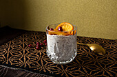 Glas mit Dessert aus Stracciatella-Mousse und Schokoladenspänen, gekrönt mit karamellisierten Orangenscheiben und Beeren neben dem Löffel