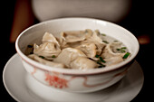 Closeup bowl of delicious soup with dumplings and spring onion against black background