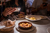 From above of crop anonymous woman taking photo of delicious food with saucy shrimps on smartphone while having dinner with boyfriend in restaurant