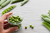 From above of cropped unrecognizable person hands peeling green pea pods on table at home