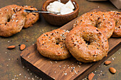 Tasty baked low carbohydrate bagels on wooden cutting board placed on table with almonds and cream cheese in light kitchen