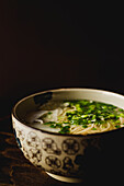 Chinese ramen meal in ceramic bowl with oriental ornament placed on wooden table on black background
