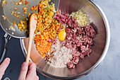 From above of crop anonymous chef adding chopped fried vegetables into bowl with minced meat and raw egg placed on gray table