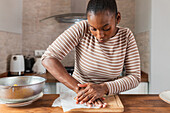Junge Afroamerikanerin zerdrückt frische Kochbananen auf einem Schneidebrett bei der Zubereitung von Patacones zu Hause