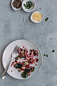 Blick von oben auf einen Teller mit leckerem Linsensalat mit Spinat und Gurken, der auf einer grauen Fläche neben Schüsseln mit Gewürzen steht