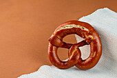 Delicious freshly baked pretzel with dark crust served on ribbed fabric against brown background