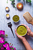 Top view composition with crop anonymous female master with bowl of died powdered henna near brush wooden comb and burning candles for natural hair care