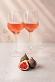 Glasses of red drink placed on table with bowl of grapes and figs