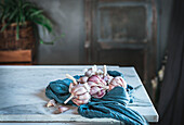 Ungeschälte Knoblauchzehen, serviert mit blauer Serviette und Keramikteller auf einem Tisch in einer hellen Küche
