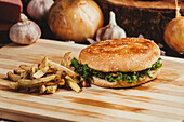 Appetizing hamburgers with vegetables placed on wooden board with French fries in kitchen