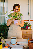 Young female florist in apron planting green plant into ceramic pot while working in professional floristry studio