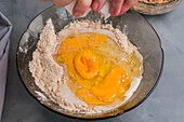 From above of crop unrecognizable person breaking raw egg into bowl with ingredients for healthy coffee keto muffins while cooking in kitchen