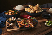 Mala-Tofu und Yuxiang, chinesische vegane Gerichte, begleitet von einer Schüssel mit Reis, Blumenkohl, Sojasauce und einer japanischen Teekanne auf einem mit Stoffen dekorierten Holztisch